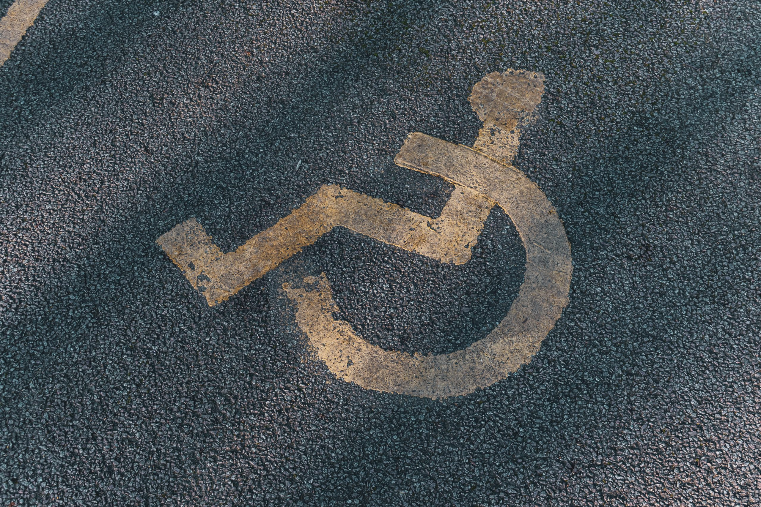 auf grauem Asphalt ist verwaschen das Symbol einem Menschen im Rollstuhl zu sehen