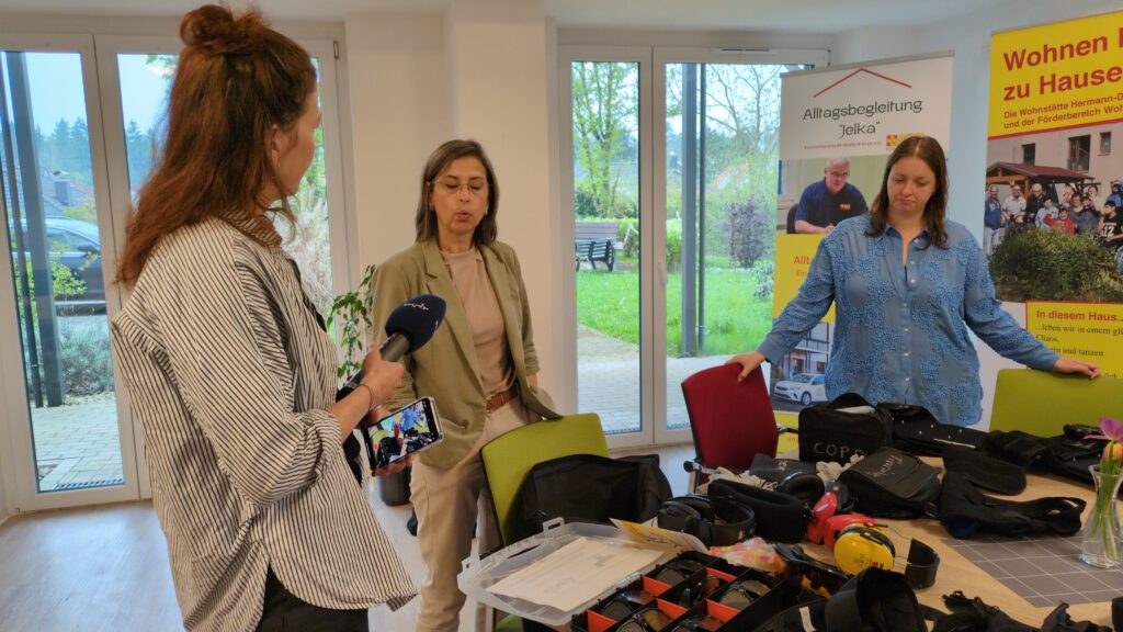 links im Bild eine Frtau, die ein Mikrofon vom MDR hält. In der Mitte steht eine Frau, die in das Mikrofon spricht. Rechts im Bild steht eine junge Frau, mit einer Hand auf eine Stuhllehne gestützt.